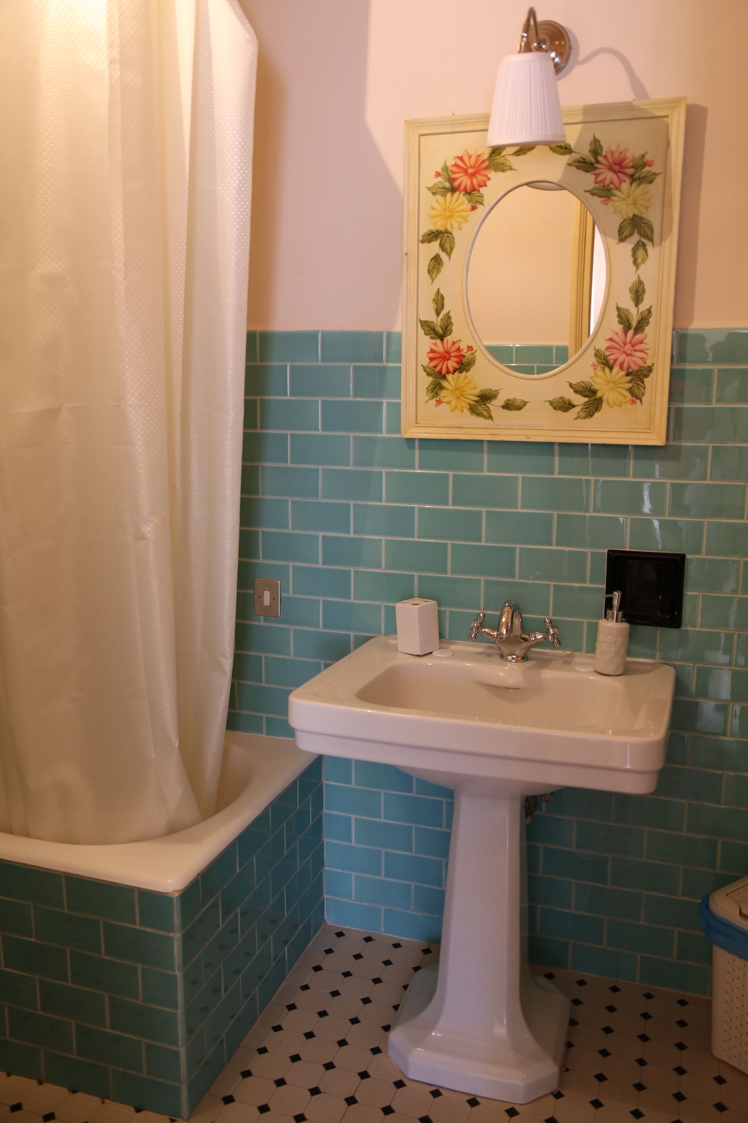 A bathroom with a white sink, a mirror with a floral frame, and a shower curtain.