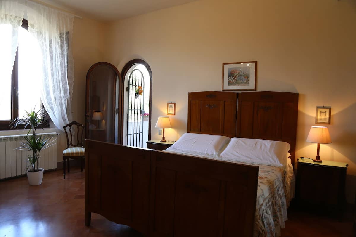 Un dormitorio con cama de madera, dos lámparas de noche, una ventana con cortinas, una silla y una planta en maceta.