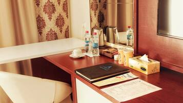 A hotel room with a wooden desk, a white chair, a laptop, a coffee maker, a kettle, bottled water, a tissue box, and a menu.
