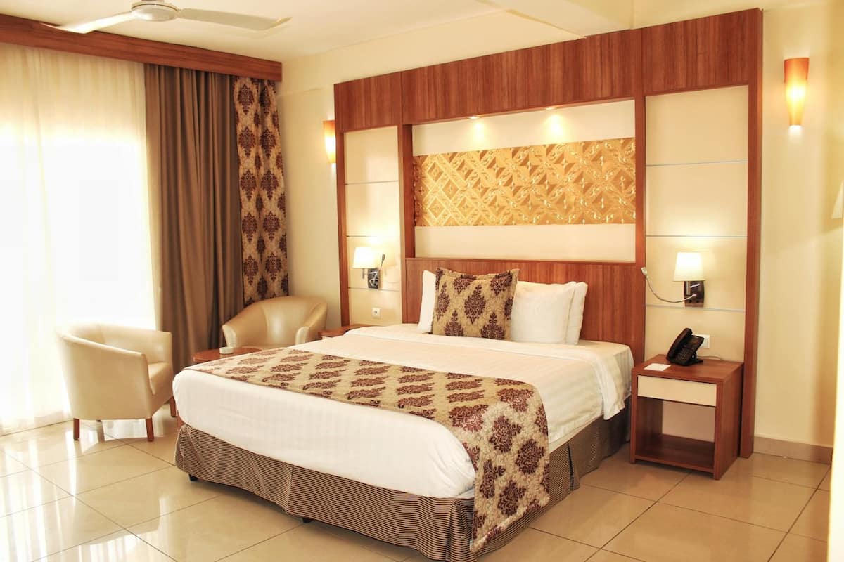 A hotel room with a large bed, a chair, a nightstand with a phone, and a wall-mounted lamp.