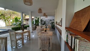 A spacious indoor area with a pool, wooden furniture, and a bookshelf with books. - Sahera Hotel (Karangasem)