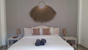 Una cama con colchón blanco, dos almohadas marrones y un cabecero. Hay dos mesitas de noche con lámparas a cada lado de la cama.