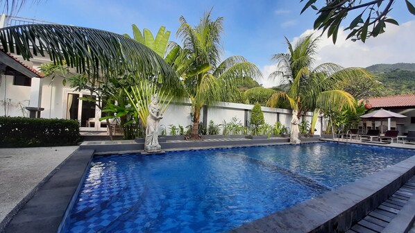 A swimming pool with a checkered pattern, surrounded by palm trees and a statue. - Sahera Hotel (Karangasem)