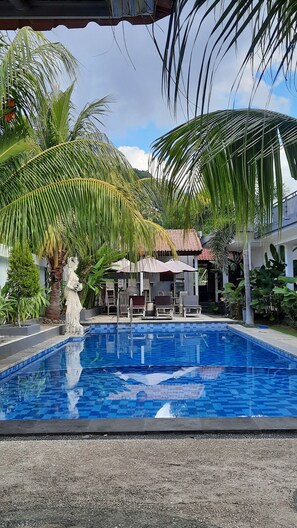 A swimming pool with a tiled deck, surrounded by palm trees and a statue. - Sahera Hotel (Karangasem)
