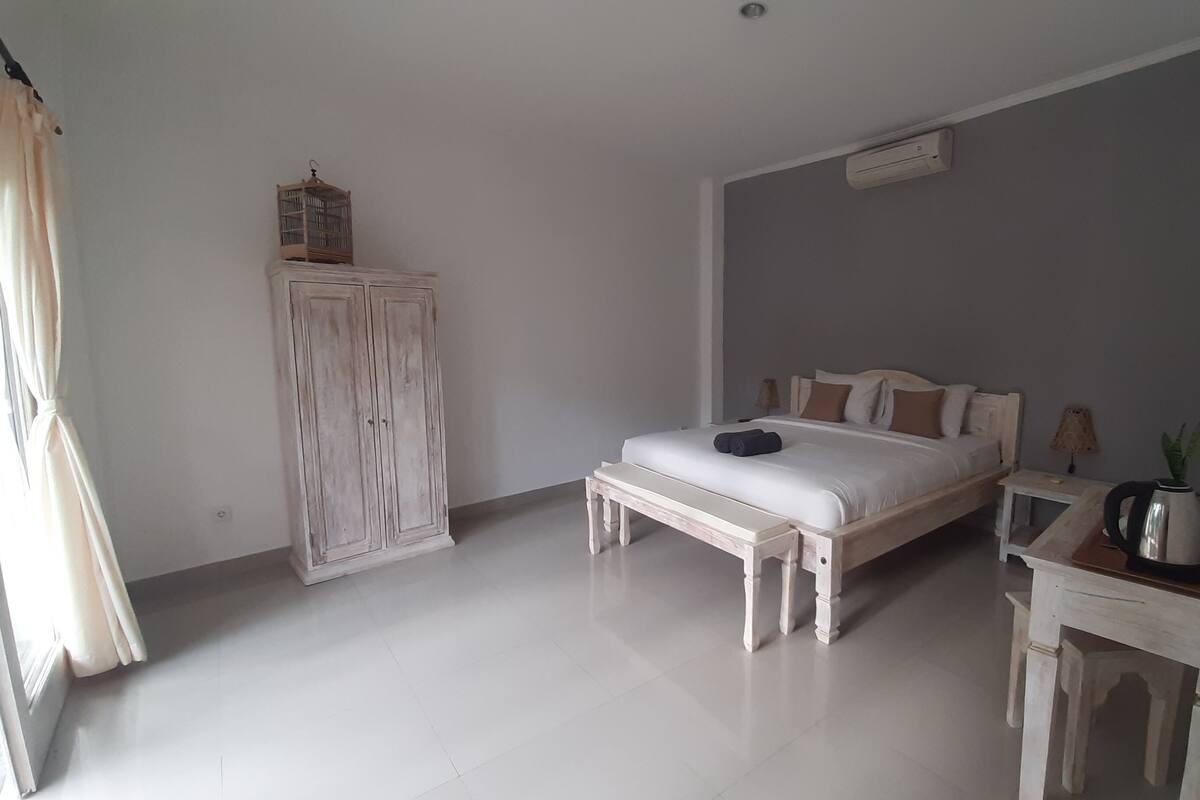 A bedroom with a bed, a wooden wardrobe, a bedside table with a lamp, and a small table with a plant.
