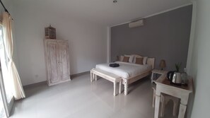 A bedroom with a bed, a wooden wardrobe, a bedside table with a lamp, and a small table with a plant. - Sahera Hotel (Karangasem)