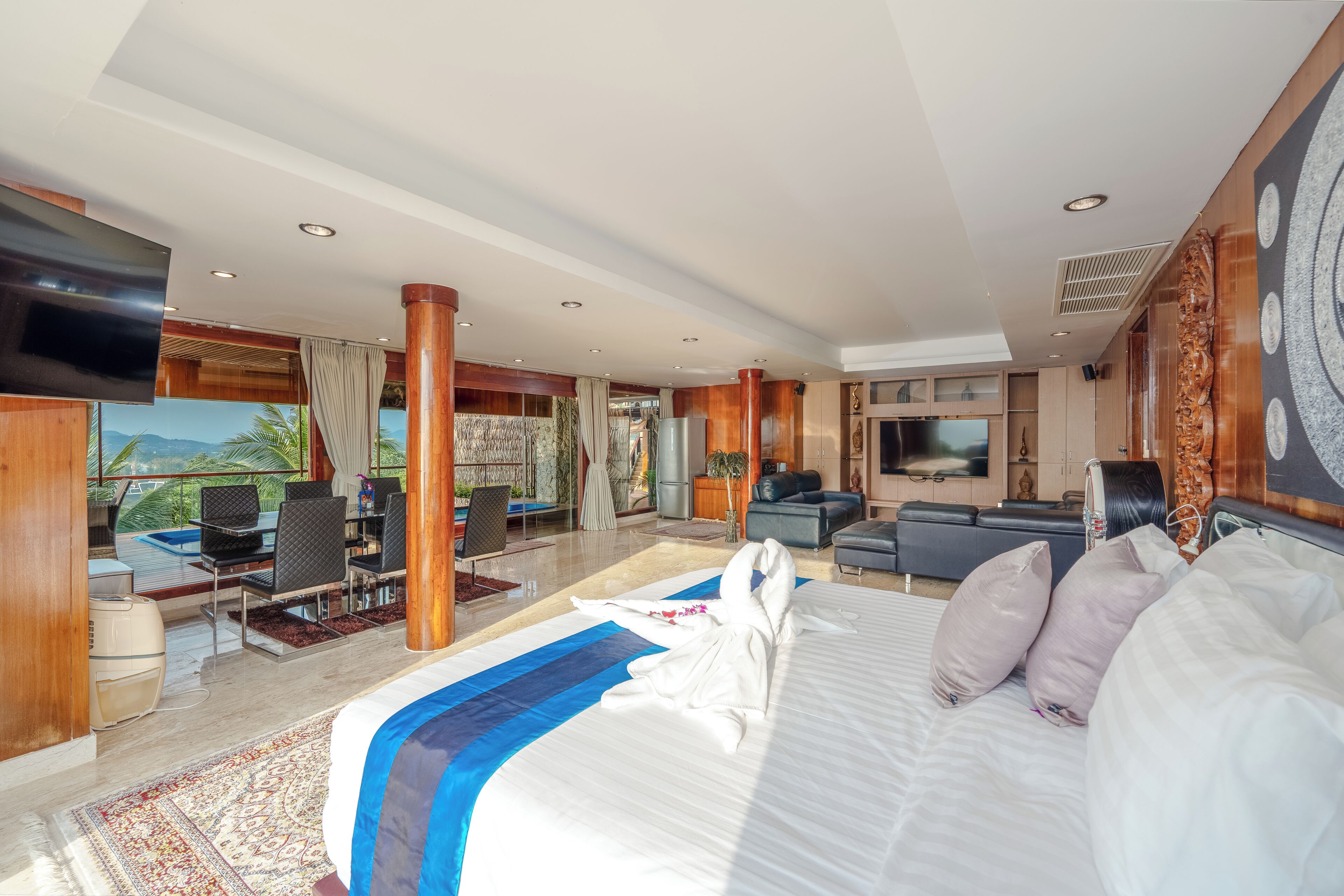 A spacious hotel room with a large bed, a TV, a seating area with a sofa and chairs, and a view of the outdoors.
