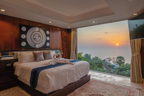A bedroom with a large bed, a view of the sunset, and a decorative wall piece.