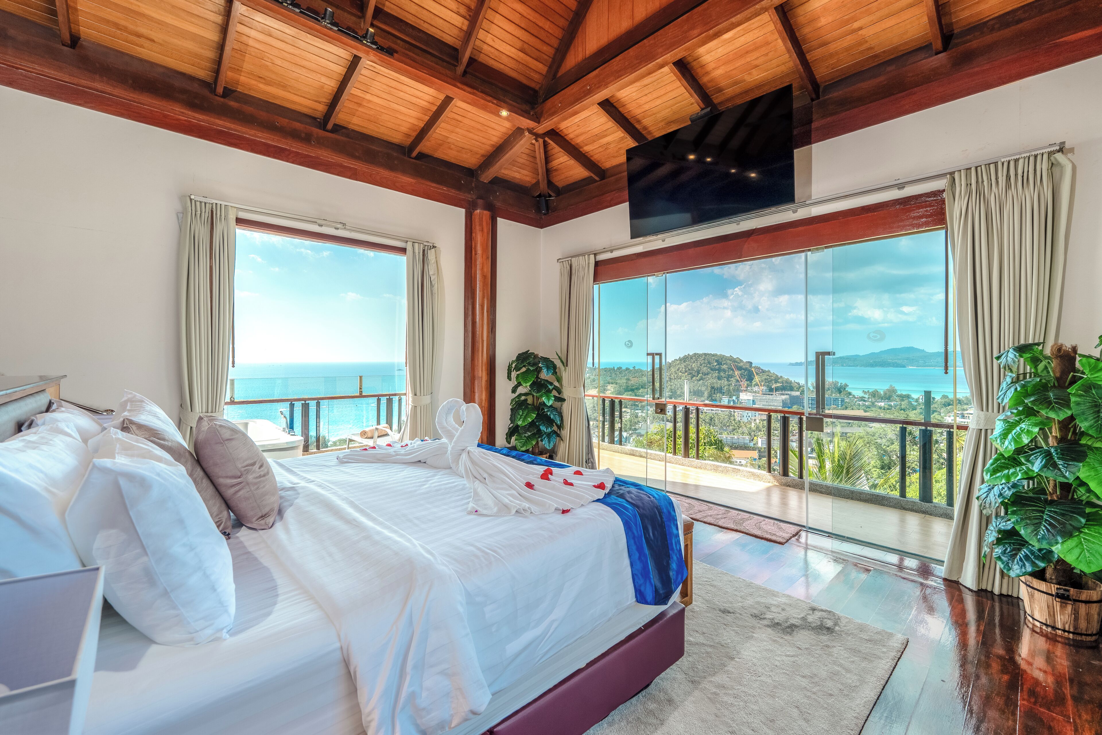 Quarto com cama grande, televisão e varanda com vista.