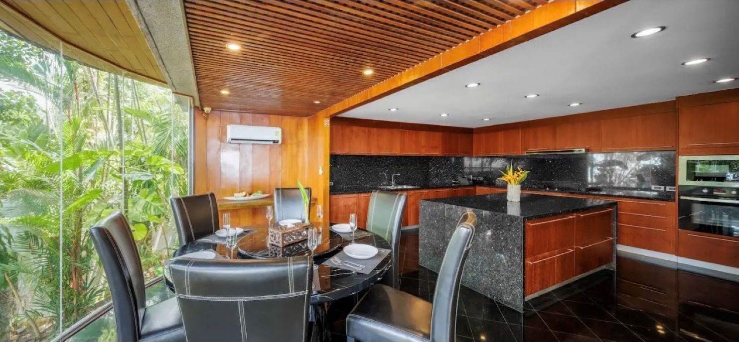 A modern kitchen with wooden cabinets, a black countertop, and a dining area with leather chairs.