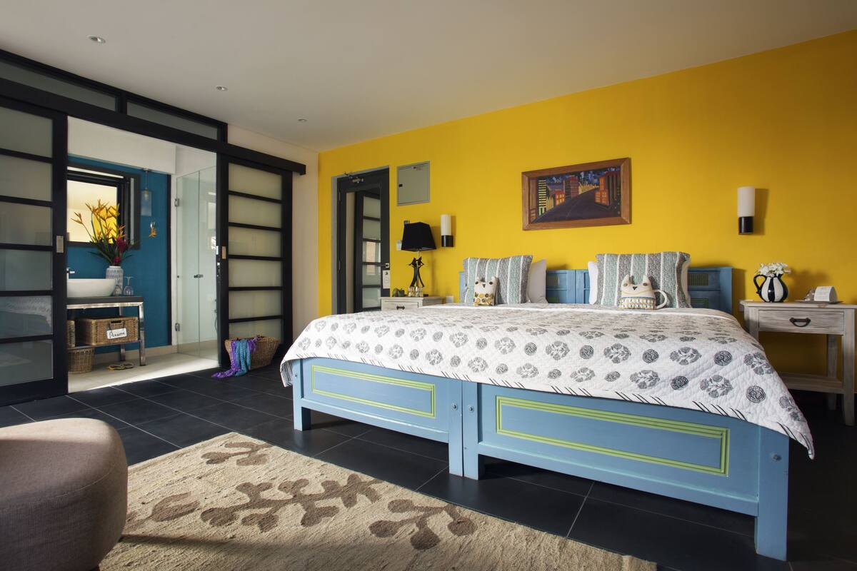 A bedroom with a bed, bedside tables, a nightstand, a lamp, a painting, and a window.