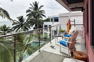 Un balcón con piscina, palmeras y vista al océano.