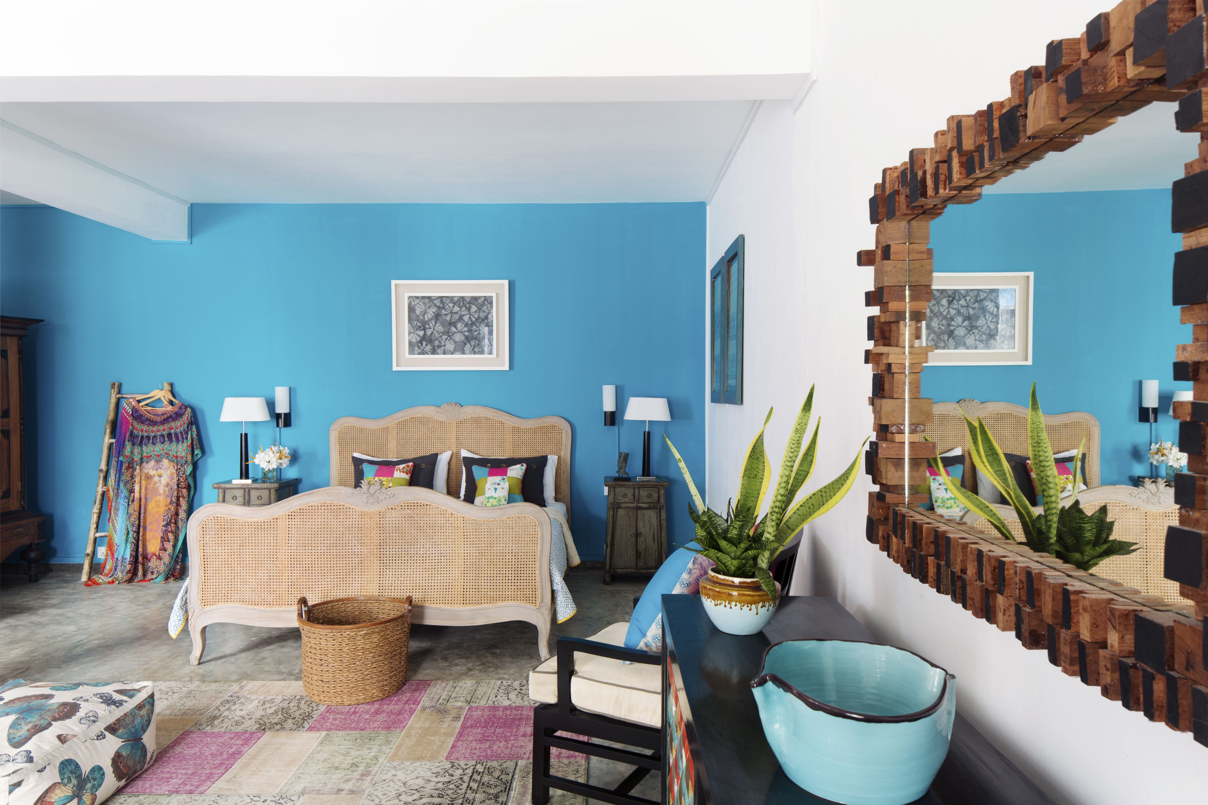 A bedroom with a blue wall, a wicker bed, a wooden headboard, a large mirror, and a potted plant.