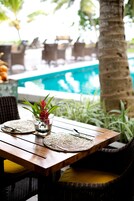 A wooden table with a woven placemat, a glass vase with a red flower, and wicker chairs with cushions.