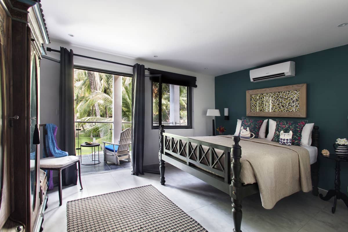 A bedroom with a bed, a window, an air conditioning unit, and a view of palm trees.