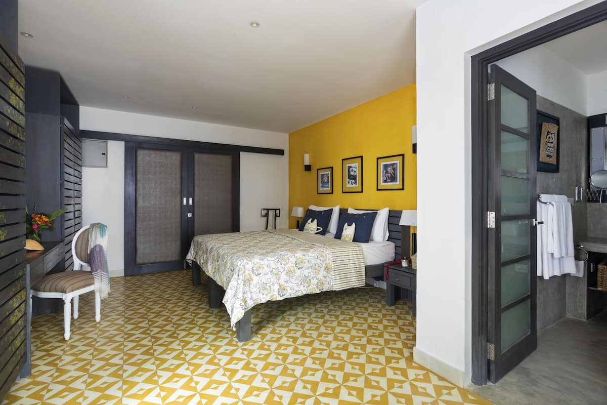 A bedroom with a bed, a chair, a bedside table, and a bathroom with a towel rack.