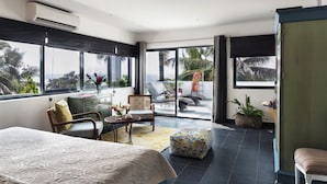 Une chambre spacieuse avec un grand lit, un coin salon comprenant un fauteuil et une petite table, et une vue sur l’extérieur grâce à une porte-fenêtre coulissante.