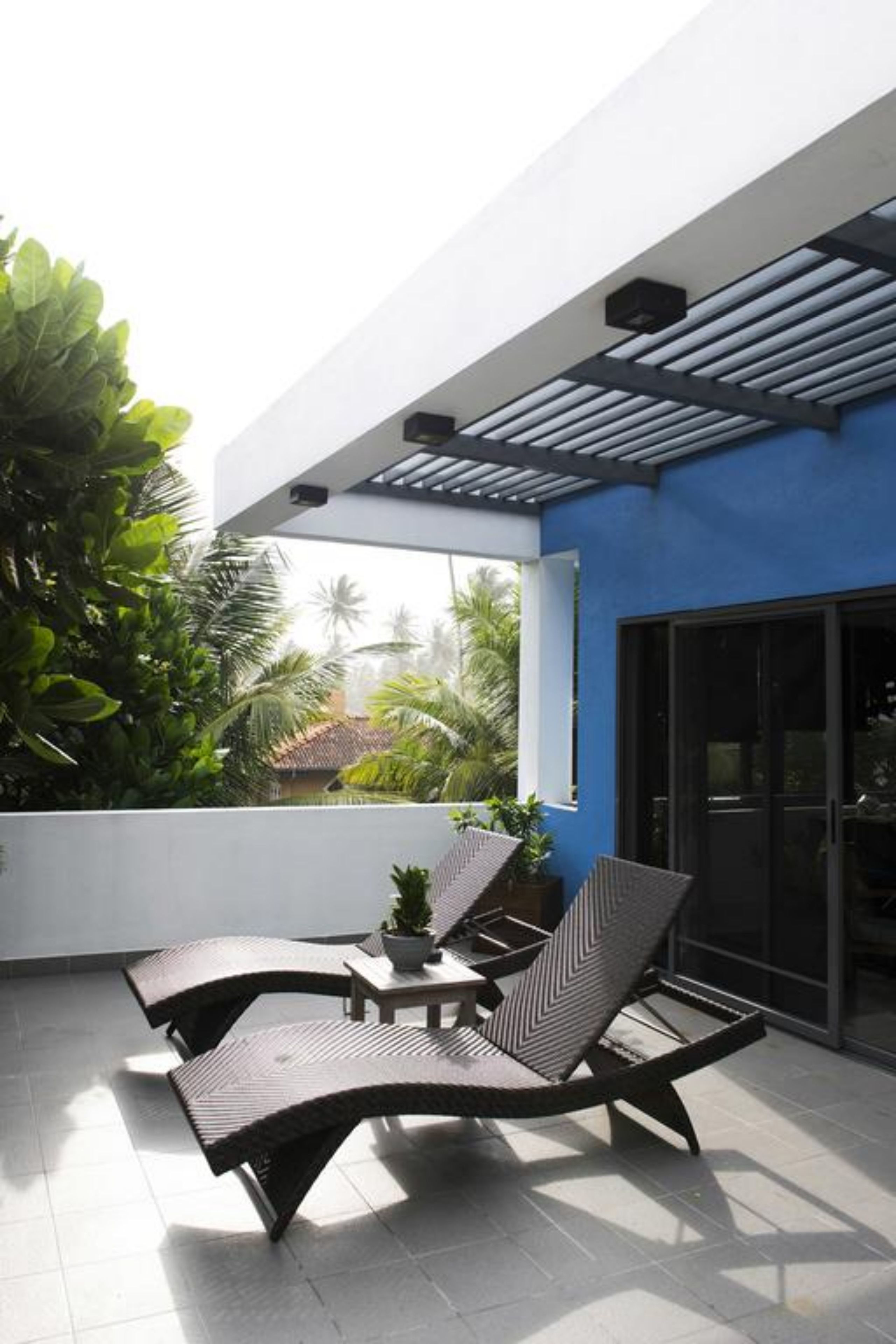 Un espace extérieur moderne, aménagé pour se détendre, avec un mur blanc et des touches de bleu, comprenant une table et deux chaises.