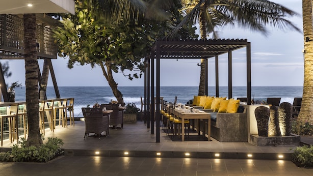 Un espace extérieur aménagé pour les repas, avec des tables et des chaises, un coin salon abrité et une vue sur l’océan.