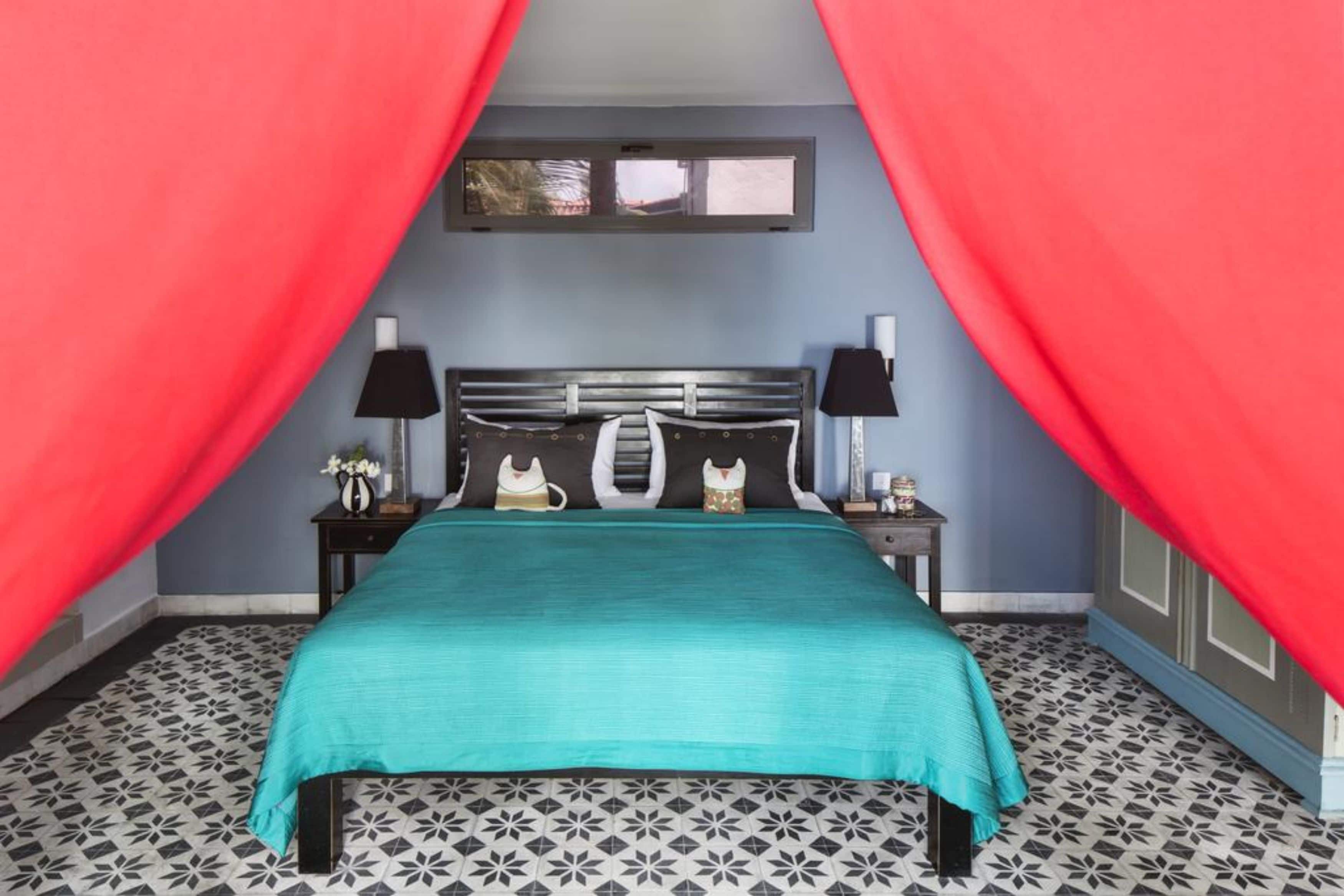 A bedroom with a bed, two bedside tables, a window, and red curtains.