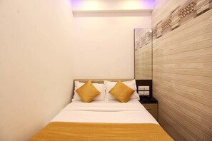 A hotel room with a bed, two pillows, a bedside table, and a wall with a decorative panel. - Hotel Golden Residency (Mumbai)