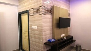 A modern interior with a flat-screen TV mounted on a wooden panel, a small shelf with a remote control, and a door with a patterned tile design. - Hotel Golden Residency (Mumbai)