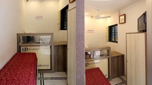 A hotel room with a reception desk, a bed with a red patterned bedspread, and a television on the wall. - Hotel Golden Residency (Mumbai)