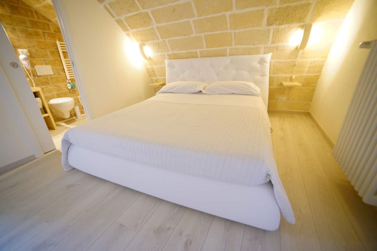 A neatly made bed in a room with a stone wall and a wooden floor.