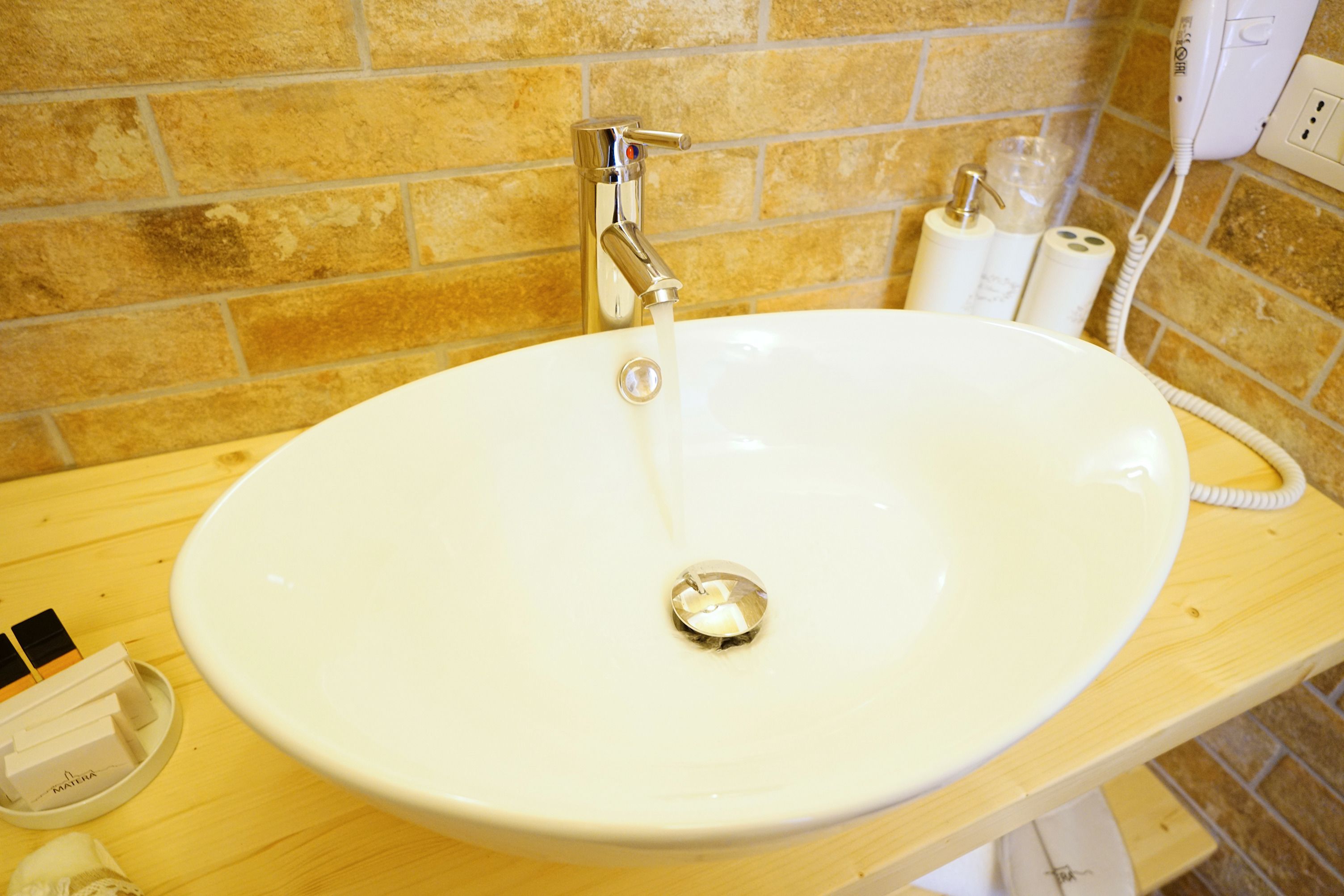 Un baño con un lavabo blanco, un grifo cromado y artículos de aseo en la encimera.