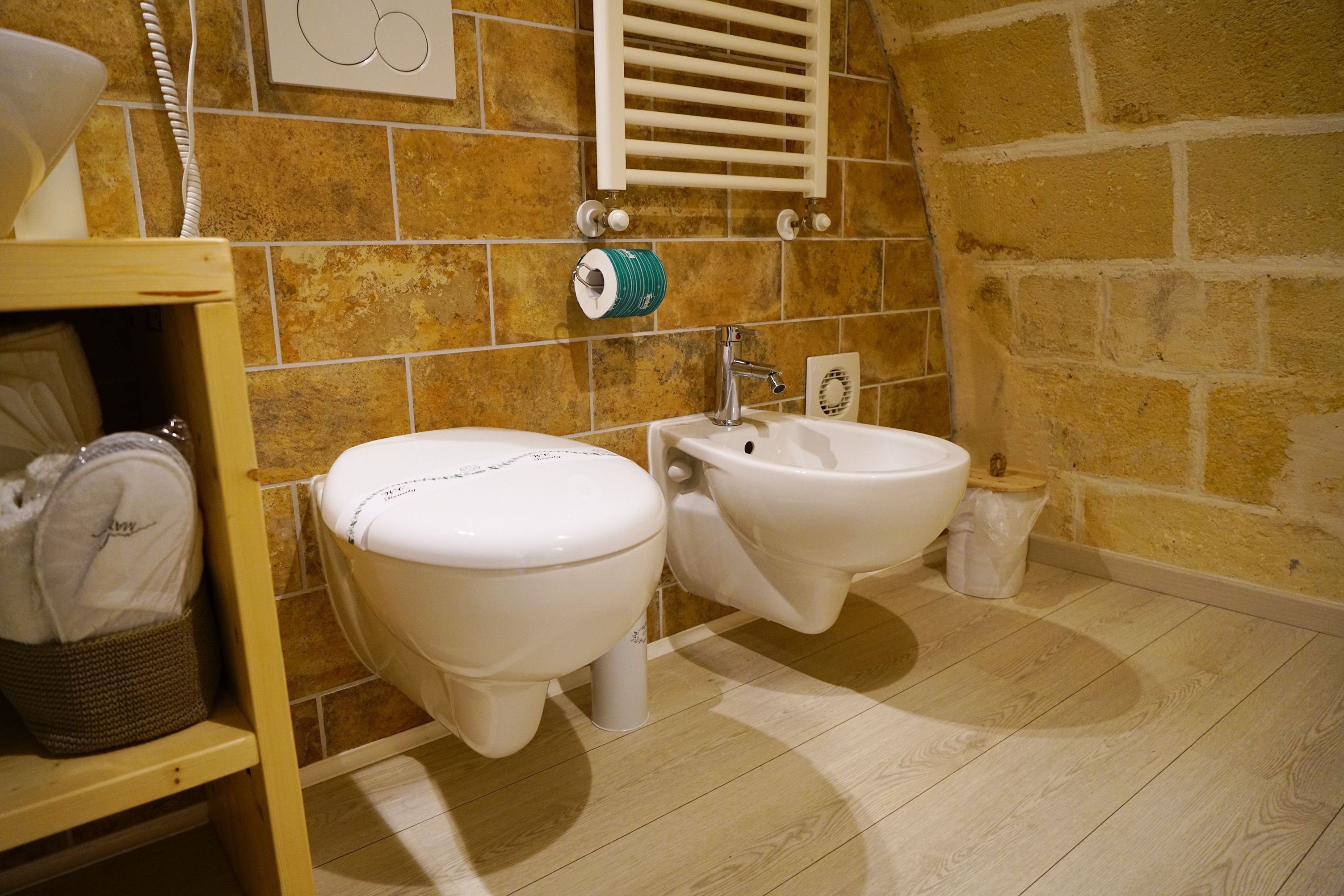 A bathroom with two toilets, a bidet, a towel rack, and a trash bin.