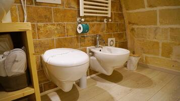 A bathroom with two toilets, a bidet, a towel rack, and a trash bin.