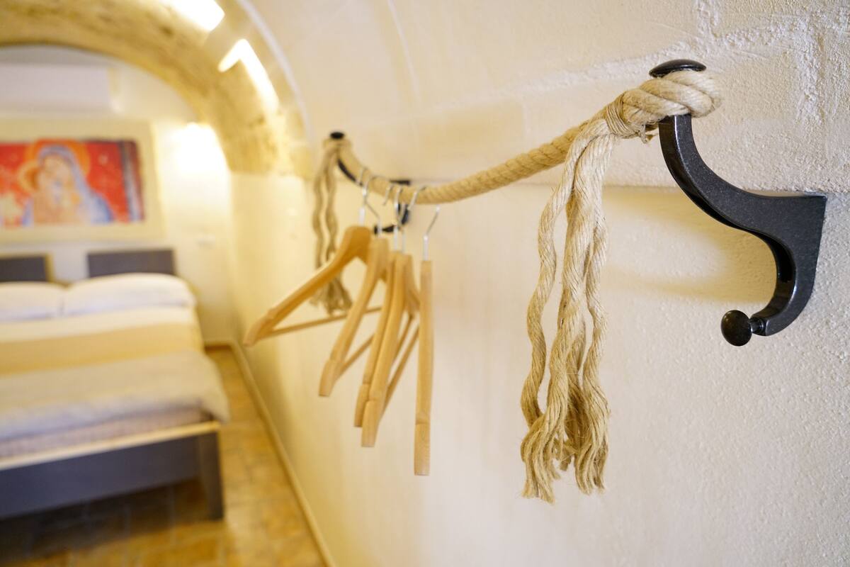 A room with a bed, a rope rack with wooden hangers, and a painting on the wall.