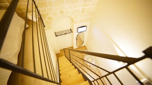 A wooden staircase with metal railings, a white wall, and a small white table with a decorative top. - La Pergola ai Sassi (Matera)