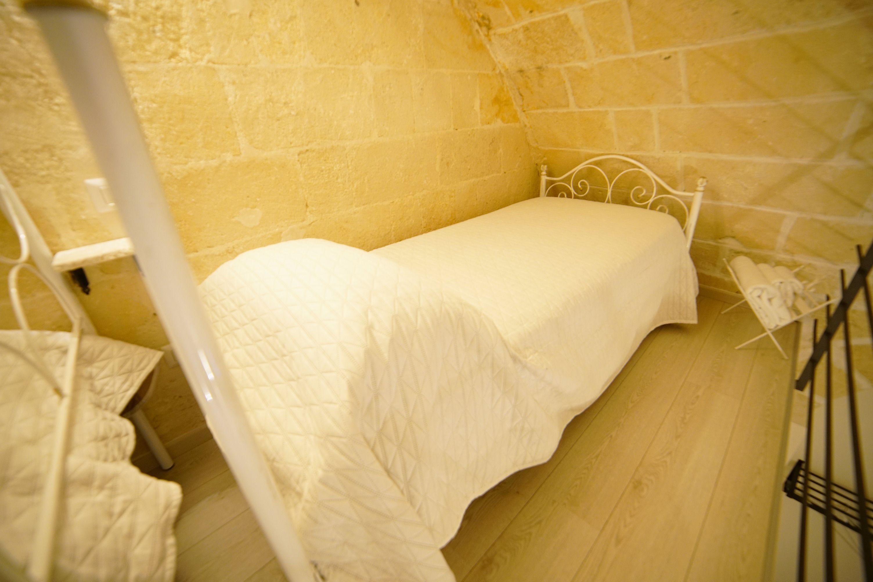 A small, single-bed room with a wooden floor and a white metal bed frame.