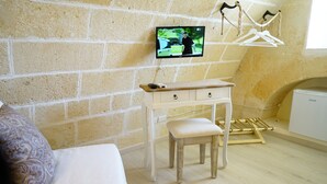 A bedroom with a brick wall, a wooden desk, a television mounted on the wall, and a hanging clothes rack. - La Pergola ai Sassi (Matera)