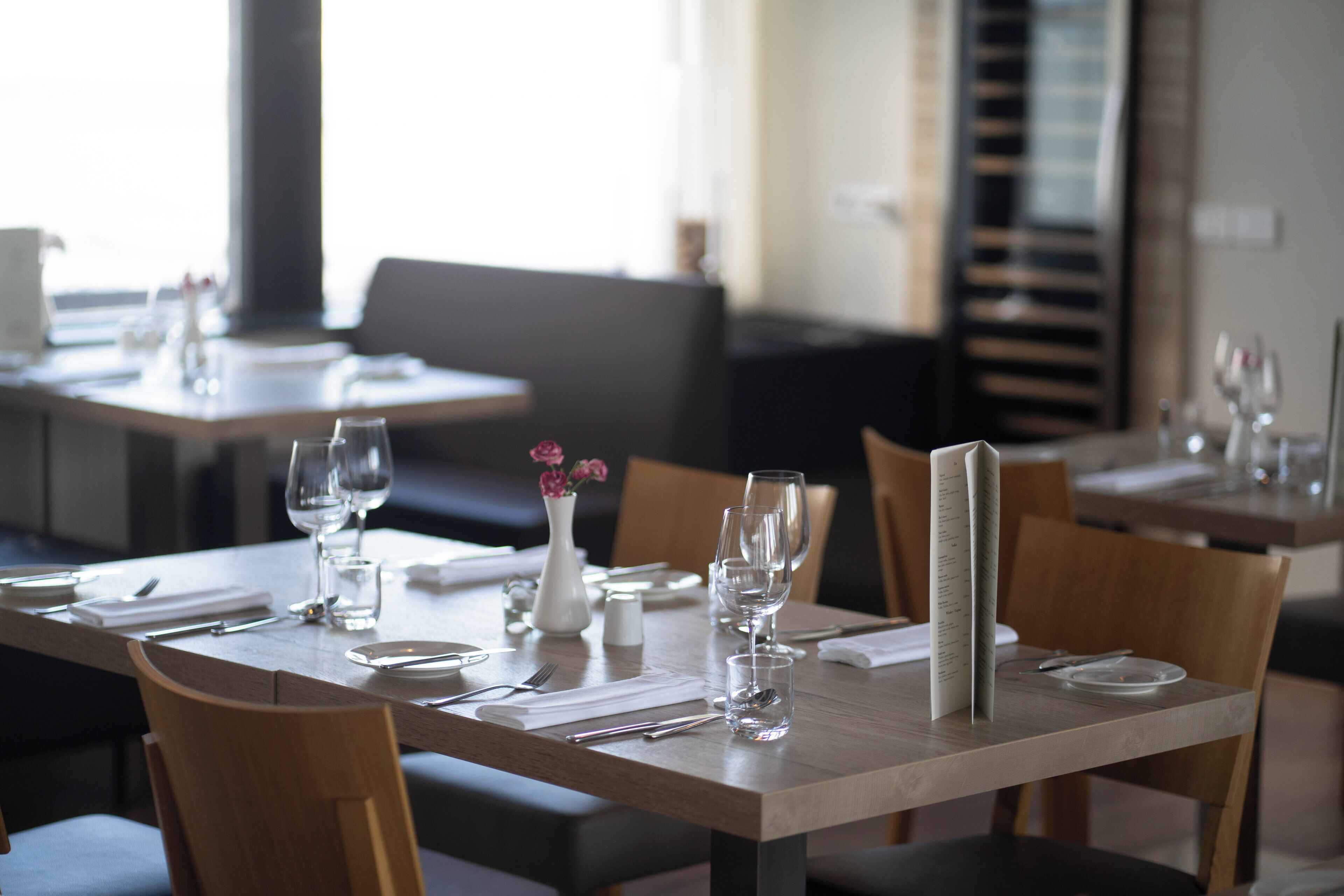 A restaurant with wooden tables and chairs, clear glassware, and a menu stand.