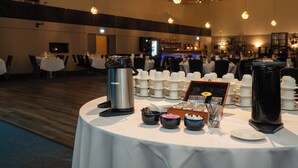 Un buffet est installé sur une table ronde dans une salle de réception, avec des distributeurs de café, des tasses et des condiments.