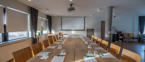 Un salón de conferencias con una larga mesa, sillas, una pantalla de proyector y un amplio ventanal.