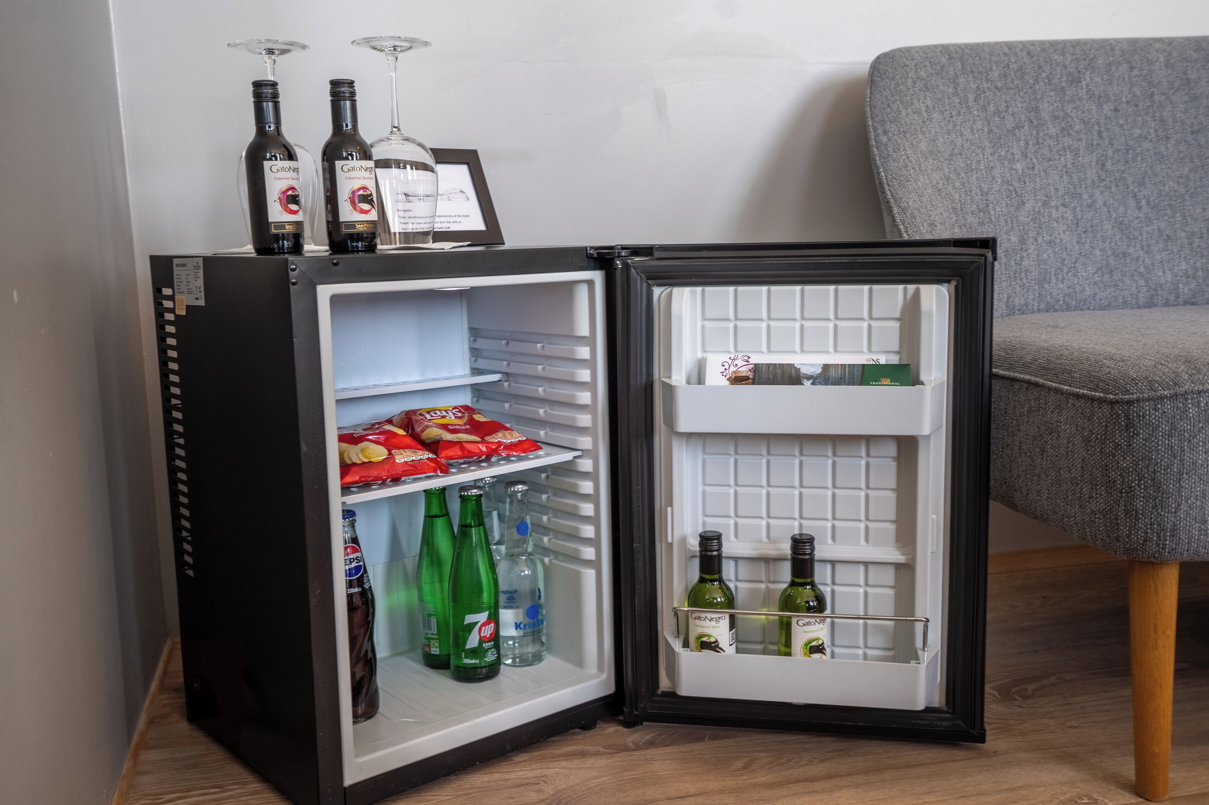 Un refrigerador pequeño negro con dos repisas, una con bocadillos y la otra con bebidas.