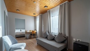 Une chambre d’hôtel moderne avec un plafond en bois, un canapé gris, une petite table, un lit et un bureau.