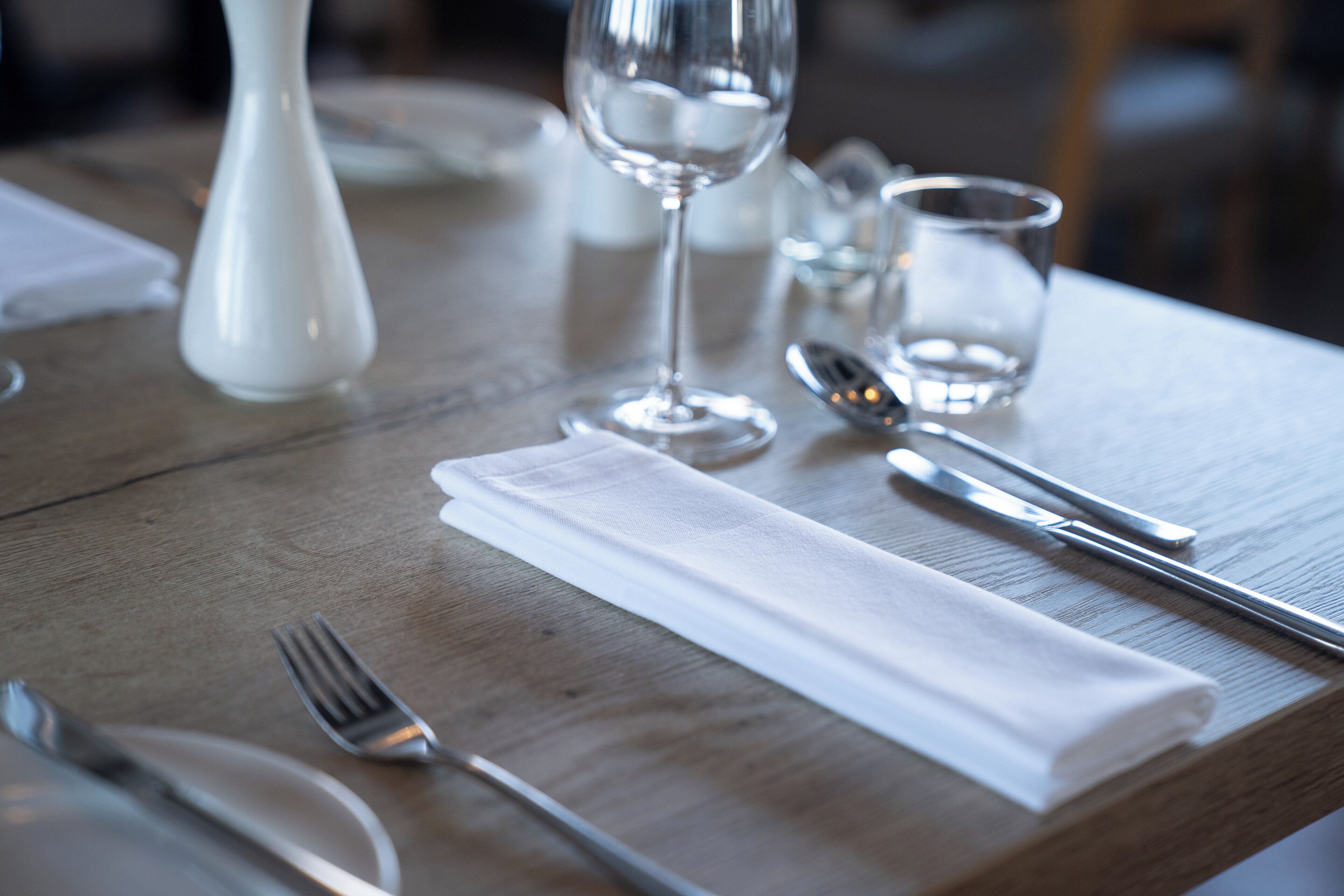 Una mesa de comedor preparada con un mantel blanco, un tenedor, un cuchillo, una copa y una copa de vino.