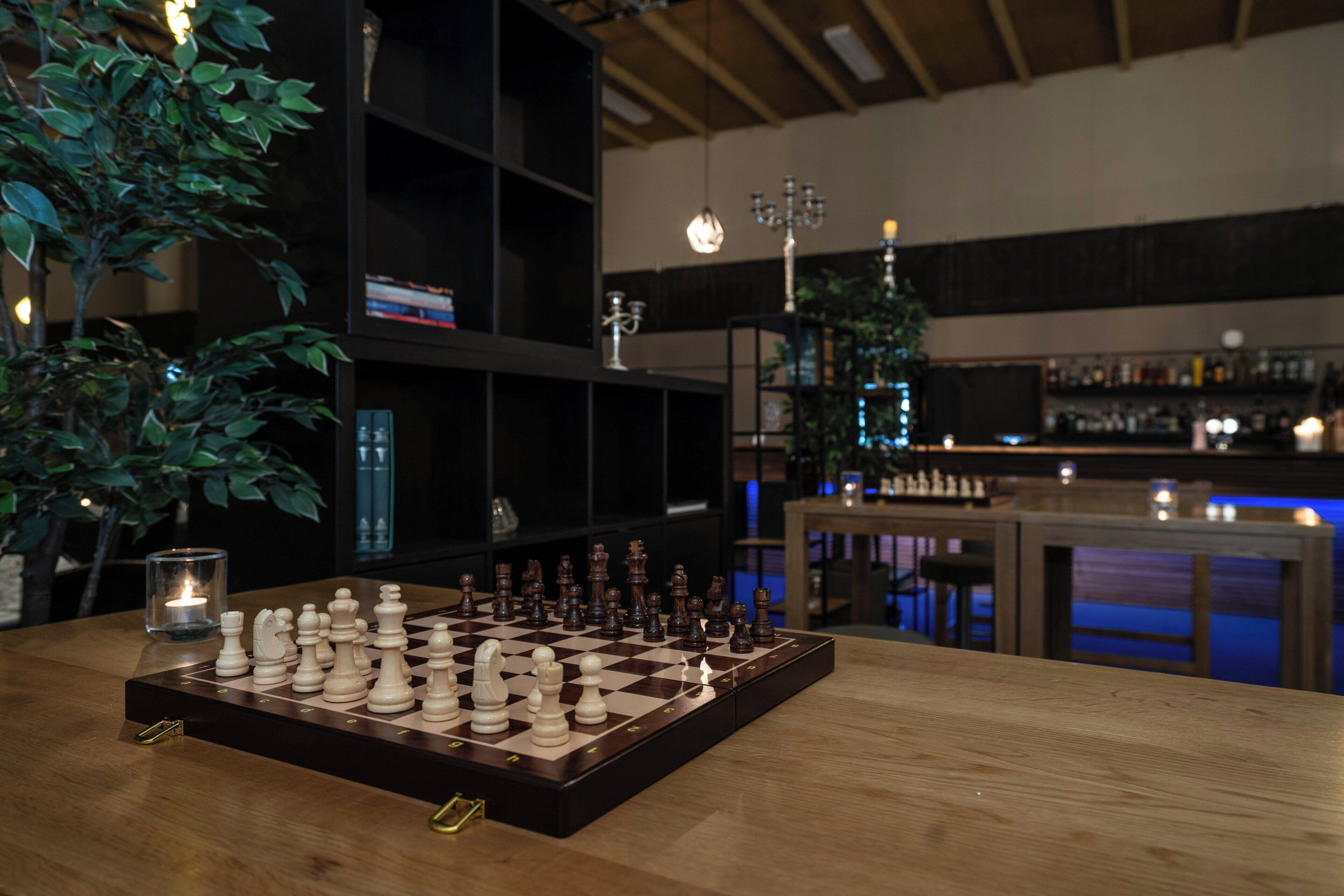 A chessboard on a wooden table with a candle and a plant nearby.