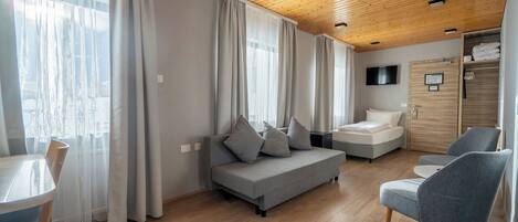 A modern room with a wooden ceiling, grey sofa, two armchairs, a dining table, and a TV on the wall.