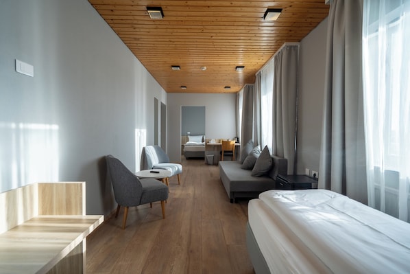 A modern hotel room with a wooden ceiling, a bed, a sofa, a chair, and a desk.