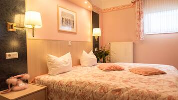A bedroom with a bed, two bedside lamps, a nightstand, a framed picture on the wall, and a window with curtains.