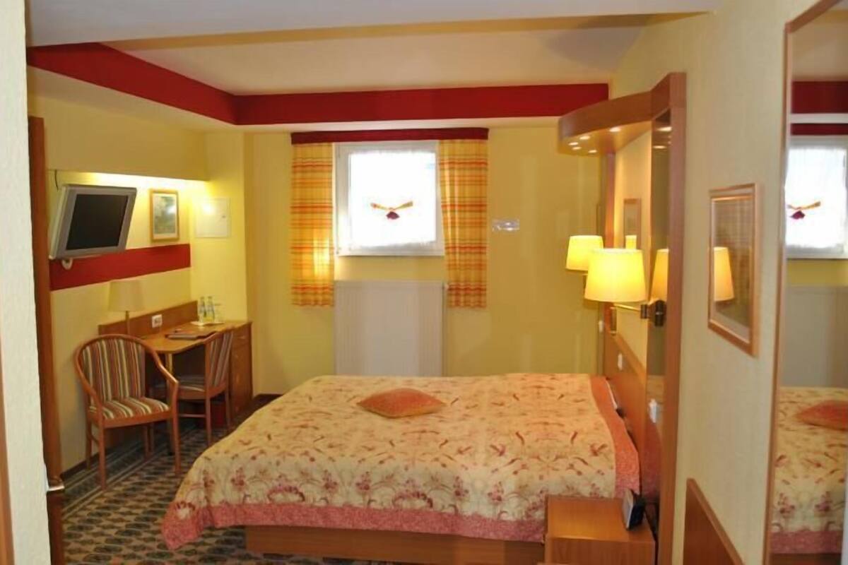 A hotel room with a bed, a desk, a chair, a television, and a window with curtains.