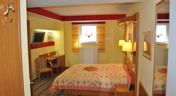 A hotel room with a bed, a desk, a chair, a television, and a window with curtains.