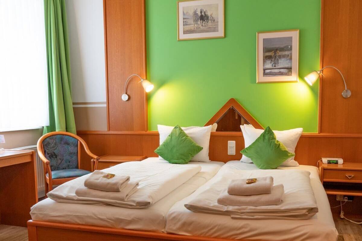 A hotel room with a wooden bed, green walls, two framed pictures, a desk, and a chair.