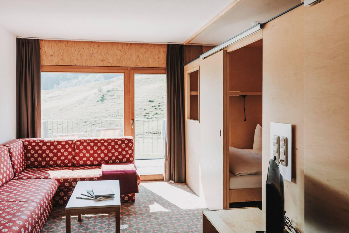 Une pièce avec un canapé rouge à motifs, une petite table et un meuble en bois.