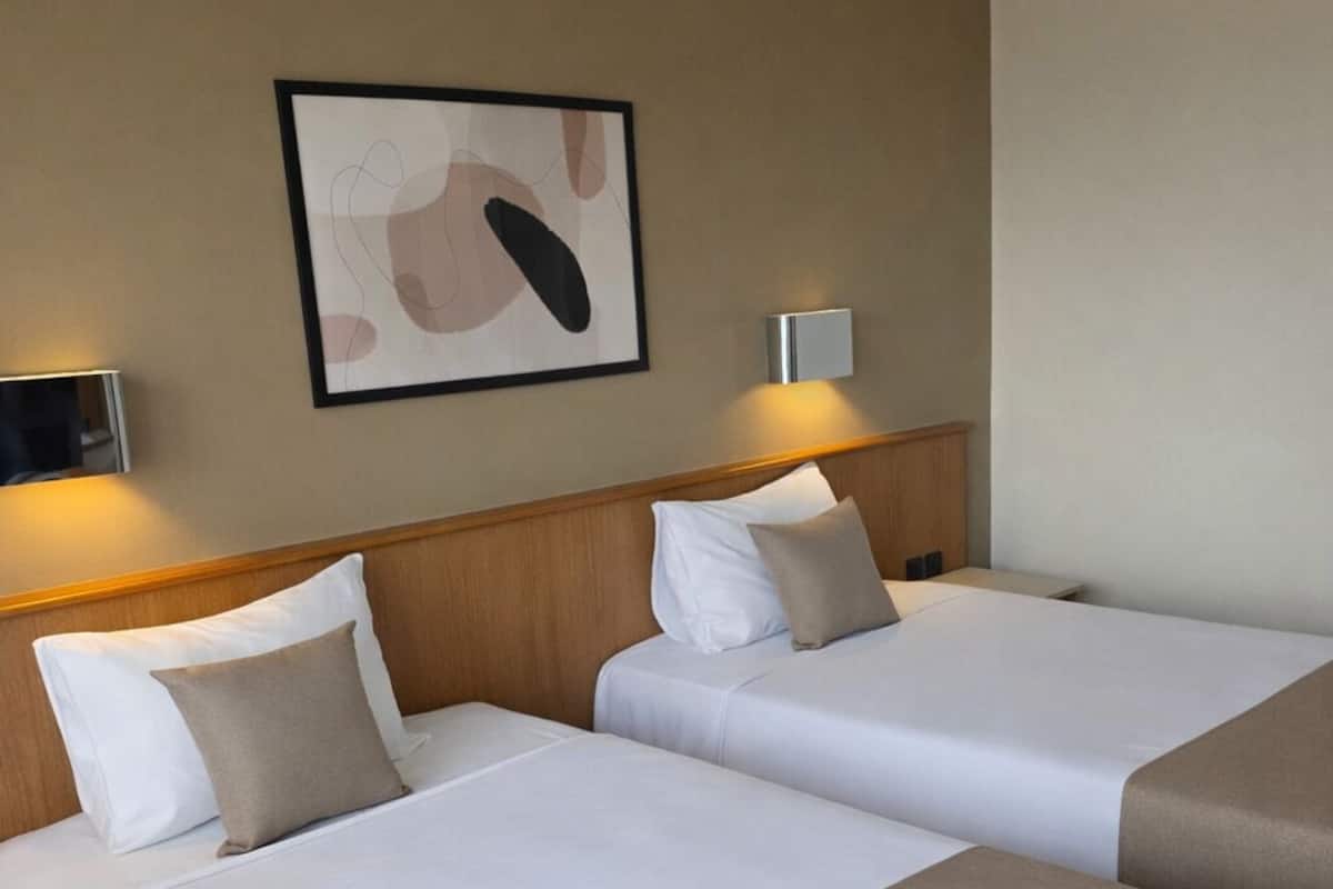 Ein Hotelzimmer mit zwei Betten, einem Kopfteil, einer Wandleuchte und einem gerahmten abstrakten Kunstwerk.